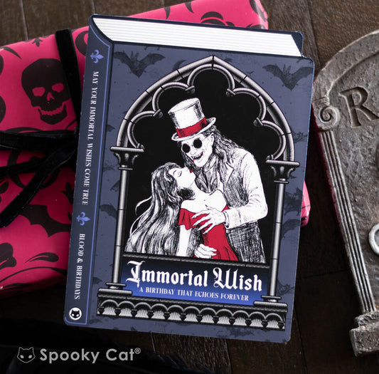 A gothic book-shaped vampire birthday card featuring a romantic undead couple in a dramatic embrace under gothic arches.