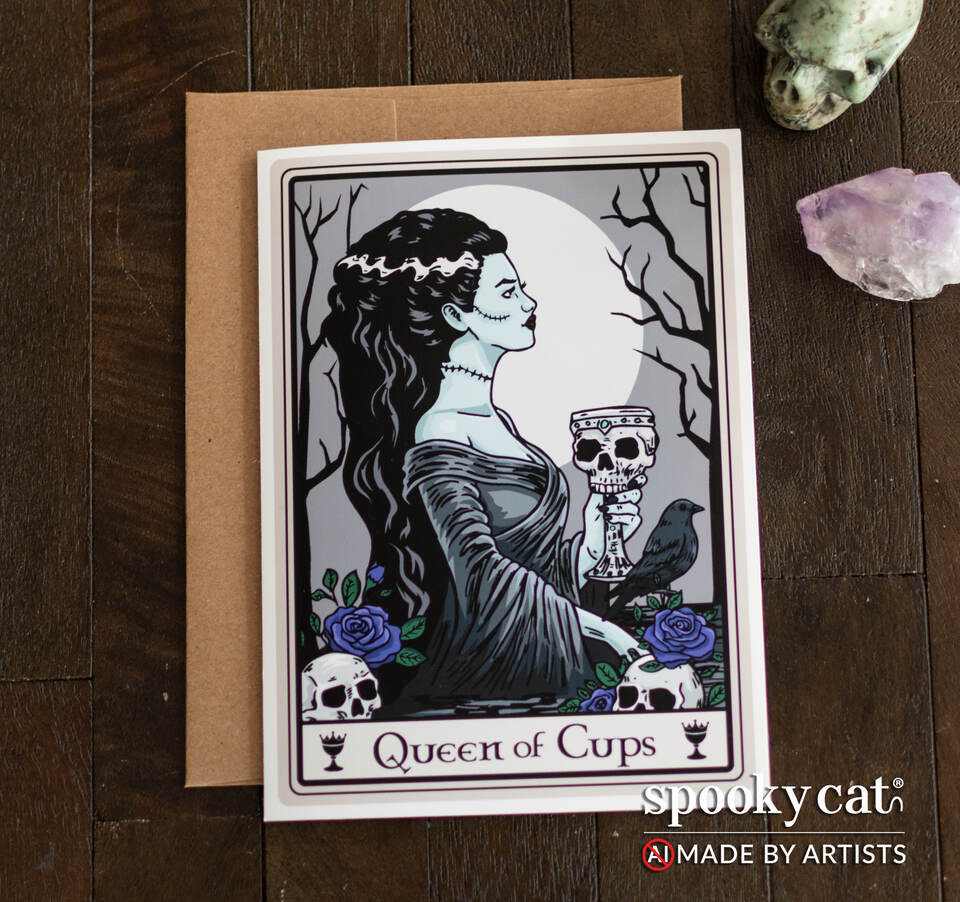 Queen of Cups tarot greeting card featuring gothic Bride of Frankenstein-inspired woman holding skull chalice with roses and raven on wood surface