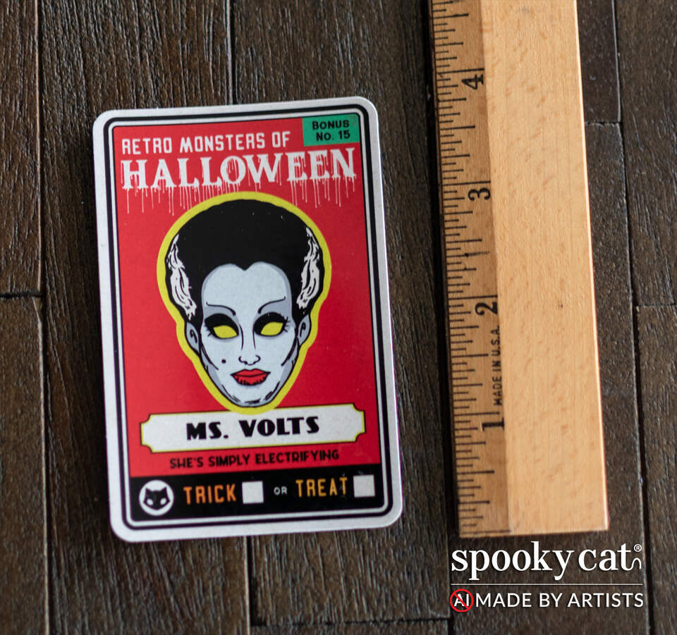 A rectangular sticker featuring a vintage-style red design with the text 'Retro Monsters of Halloween' and 'Ms. Volts,' shown on a dark wood surface next to a wooden ruler.