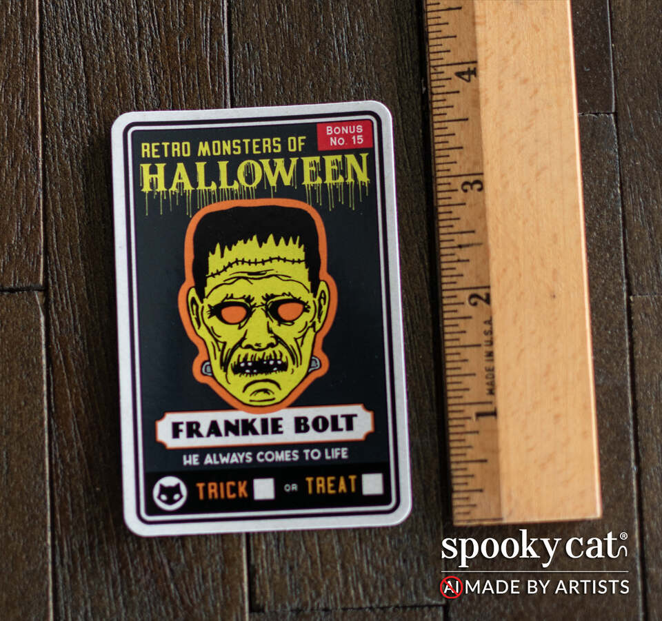 A rectangular novelty sticker featuring a Frankie Bolt horror character on a black background, placed on a dark wood surface next to a wooden ruler for scale. The card reads 'Retro Monsters of Halloween' and 'Frankie Bolt.