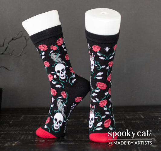 Black socks with red gothic roses and skulls, Spooky Cat Press's signature Queen of Thorns pattern worn on a foot mannequin