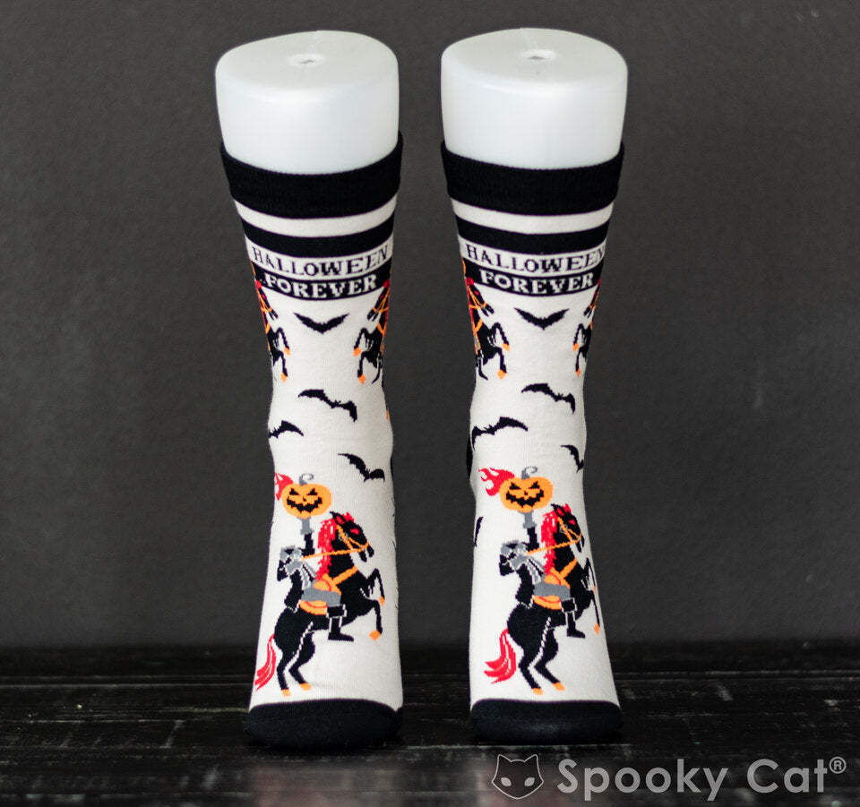 Front view of novelty Halloween socks featuring the Headless Horseman riding a black horse with red accents, surrounded by flying bats. The cuff reads "Halloween Forever" — spooky Sleepy Hollow-themed socks by Spooky Cat Press.
