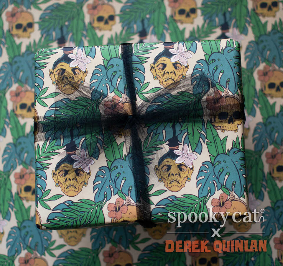 Wrapped gift box featuring Spooky Cat Press x Derek Quinlan tropical horror gift wrap with shrunken heads, monstera leaves, hibiscus flowers, and tiki-inspired spooky artwork on a cream background.