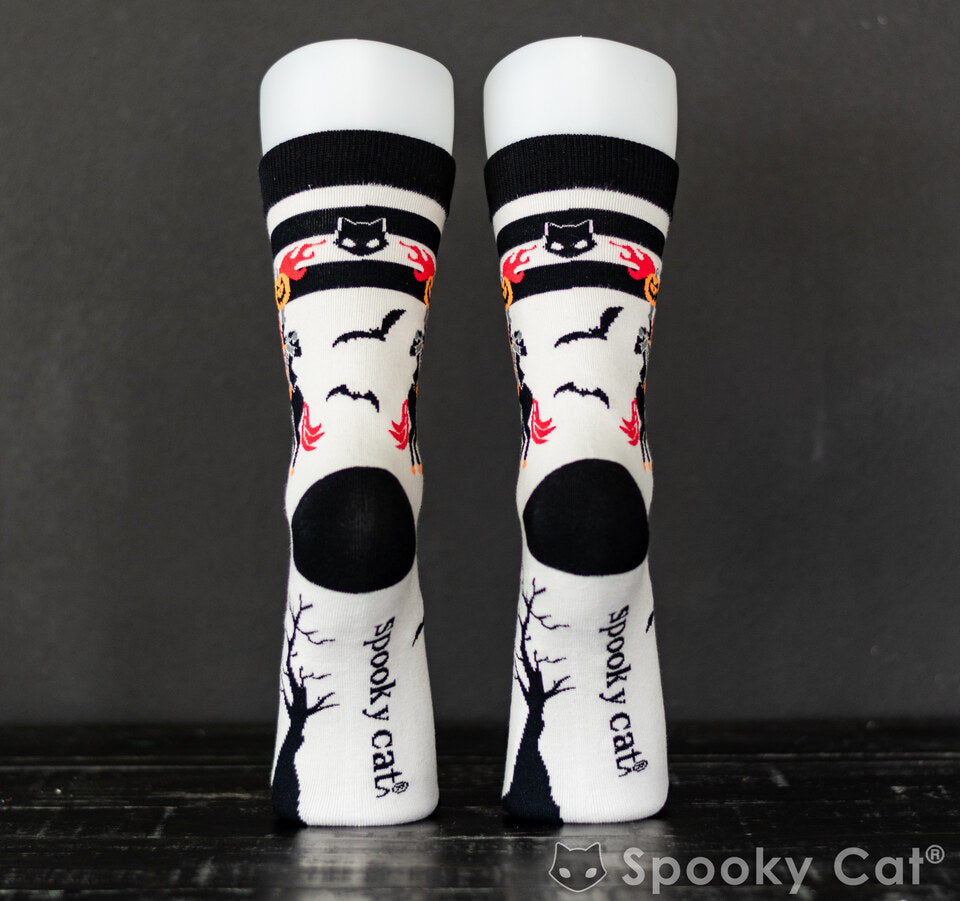 Back view of Halloween-themed socks with "Spooky Cat" branding on the heel and a spooky tree silhouette. The top band features a black cat face flanked by flames and pumpkins—Sleepy Hollow vibes meet cozy Halloween fashion.