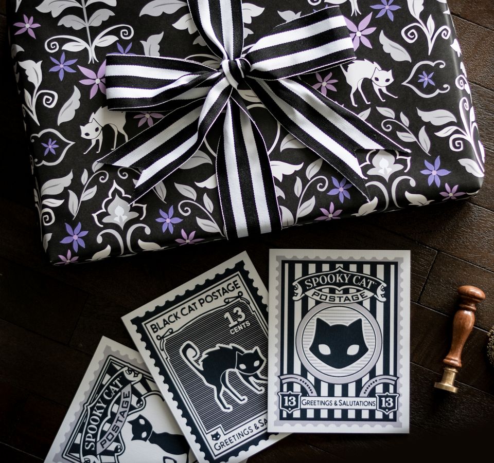 Spooky Cat Postage greeting card set displayed with gothic decor, including four vintage black cat stamp-style cards and a black cat statue.