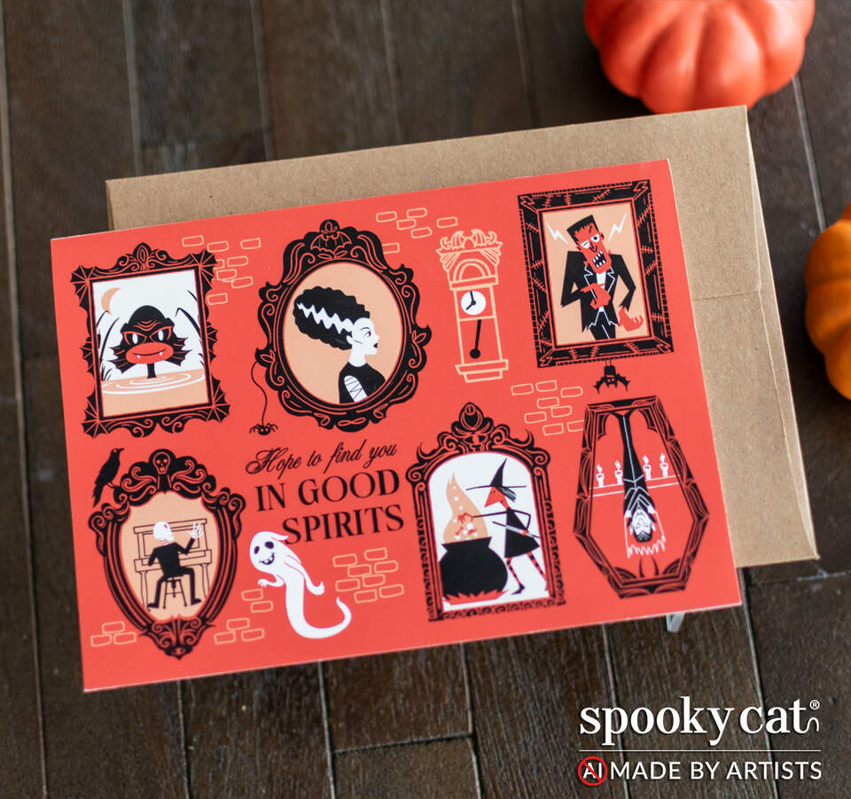 A Halloween greeting card with a red-orange background and vintage-style illustrations of ghosts and classic monsters drawn in frames. Card is placed on top of a brown kraft envelope on a dark wood surface. Pumpkins are partially visible in the background, and the Spooky Cat brand logo appears in the bottom right corner with the text NO AI, made by artists.