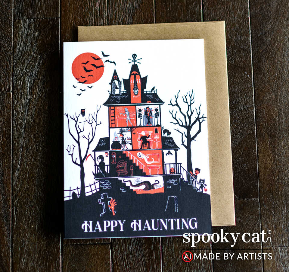 A Halloween greeting card with an orange, black, and white haunted house featuring witches, ghosts, trick or treaters and more! The words Happy Haunting are shown at the bottom of the card. Card is placed on top of a brown kraft envelope on a dark wood surface and the Spooky Cat brand logo appears in the bottom right corner with the text NO AI, made by artists.
