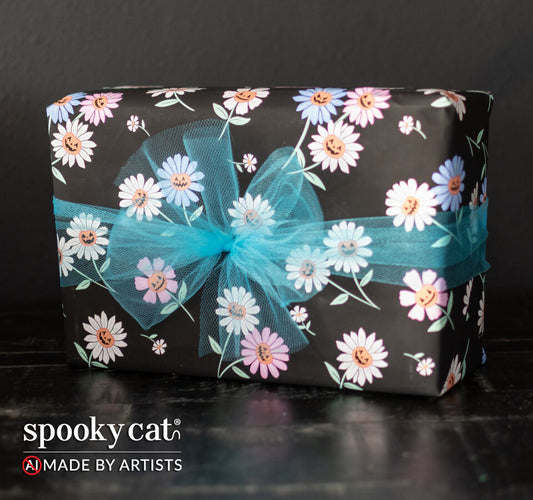 Gift wrapped in black Springoween floral wrapping paper with pastel daisies featuring small pumpkin faces in the centers, tied with a teal tulle bow.