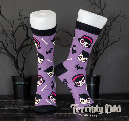 Terribly Odd Coffin Kid socks featuring a boy and girl, bats, bones, and tombstones on a purple background worn on a foot mannequin.