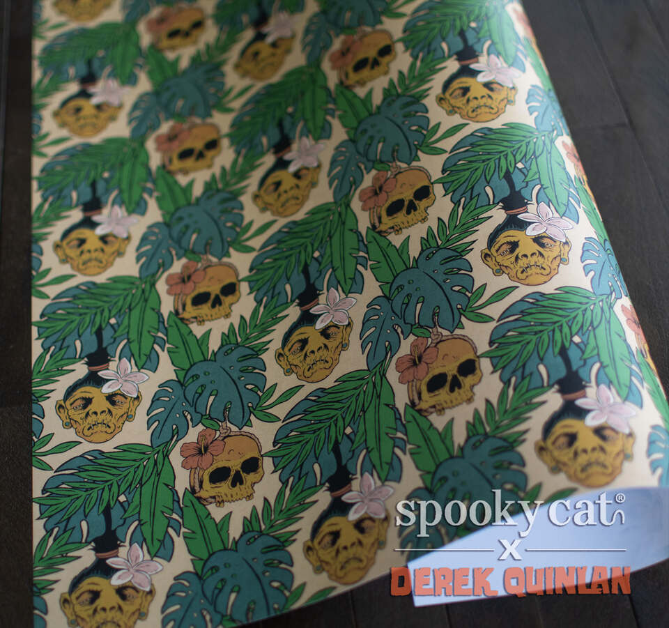 Premium spooky tiki gift wrap featuring shrunken skulls, tropical monstera leaves, palm fronds, and hibiscus flowers in a vintage island horror pattern by Derek Quinlan.